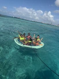 A lively group enjoys a fun day in the water, relaxing on a floating mat in the beautiful turquoise sea — perfect for summer adventures and water activities.