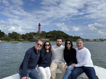 A cheerful group poses on a boat with a picturesque lighthouse in the background, capturing a memorable day on the water.
