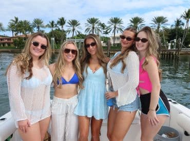 A fun group of friends poses for a cheerful photo on a boat, showcasing their stylish swimwear and sunglasses — perfect for a day out on the water.