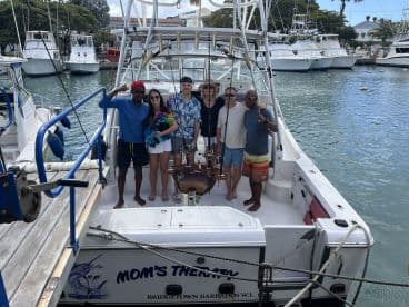 A cheerful group poses aboard the 'Mom's Therapy' boat in Bridgetown, Barbados, ready for a day of fishing and fun on the water.