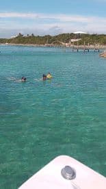 A group of snorkelers, including a child in a colorful life jacket, enjoy swimming in the crystal-clear waters, making for a perfect family adventure in a tropical paradise.
