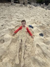 A child enjoys a playful moment at the beach, covered in sand and having fun — a perfect snapshot of beachside adventures.
