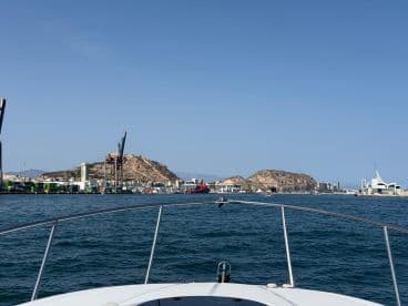 A scenic view from the bow of a boat, showcasing the harbor and coastline with cranes and hills in the background — perfect for capturing the beauty of coastal adventures.
