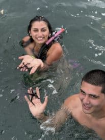 Two snorkelers joyfully interact with starfish while swimming in the ocean, showcasing a fun wildlife experience in a tropical setting.