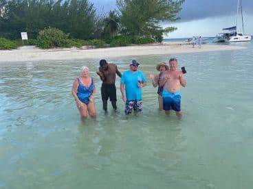 A lively group enjoys a fun day at the beach, wading in shallow waters with a catamaran anchored nearby — perfect for memorable island adventures.