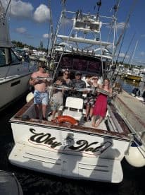 A joyful group poses with their catch aboard the 'Why Not' boat, celebrating a successful fishing trip at the marina.