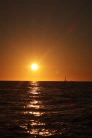 A stunning sunset over the ocean with a sailboat silhouetted against the vibrant sky, creating a picturesque scene perfect for romantic evening cruises.