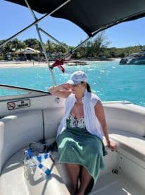 A woman relaxes on the seating of a boat, with snorkel gear nearby, enjoying the beautiful turquoise waters and beach scenery.