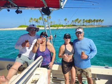 A cheerful group enjoys drinks on a boat, surrounded by stunning turquoise waters and a picturesque island backdrop — perfect for a fun day out on the water.