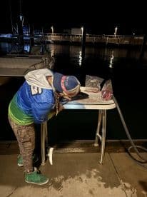 A young angler prepares their catch at a dockside table under the night sky, showcasing the excitement of a fishing adventure.