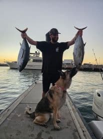 A proud angler displays his impressive catch of fish at sunset, accompanied by his loyal dog on the dock — a perfect moment celebrating a successful fishing trip.