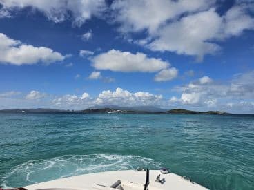 A scenic view from the bow of a boat, showcasing the vibrant turquoise waters and a picturesque island backdrop under a bright blue sky.