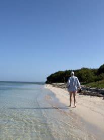 A person strolls along a serene beach, enjoying the clear waters and beautiful scenery — a perfect escape for beach lovers.