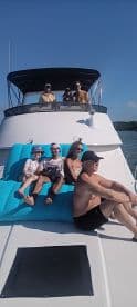 A lively group enjoys a sunny day on a boat, relaxing on a large float while soaking up the sun — perfect for a fun day out on the water.