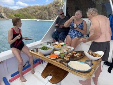 A lively group enjoys a delicious meal aboard a boat, showcasing a variety of snacks and dishes — perfect for a fun day on the water.