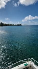 A serene view of a boat's bow cutting through crystal-clear waters, showcasing the beautiful coastline and vibrant blue skies — perfect for a day of exploration on the water.