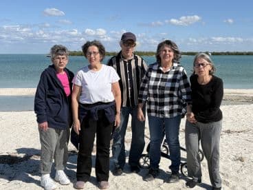 A cheerful group of friends poses together on the beach, enjoying a sunny day by the water — perfect for creating lasting memories.