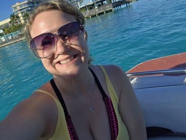 A joyful woman takes a selfie on a boat with vibrant turquoise waters in the background, capturing the essence of a fun day on the water.