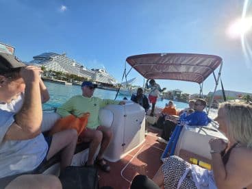 A lively group enjoys a boat cruise, surrounded by beautiful scenery and a large cruise ship in the background, perfect for a fun day on the water.