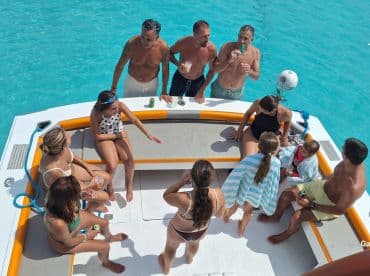 A lively group enjoys drinks and conversation aboard a boat in crystal-clear waters, perfect for a fun day on the water with family and friends.