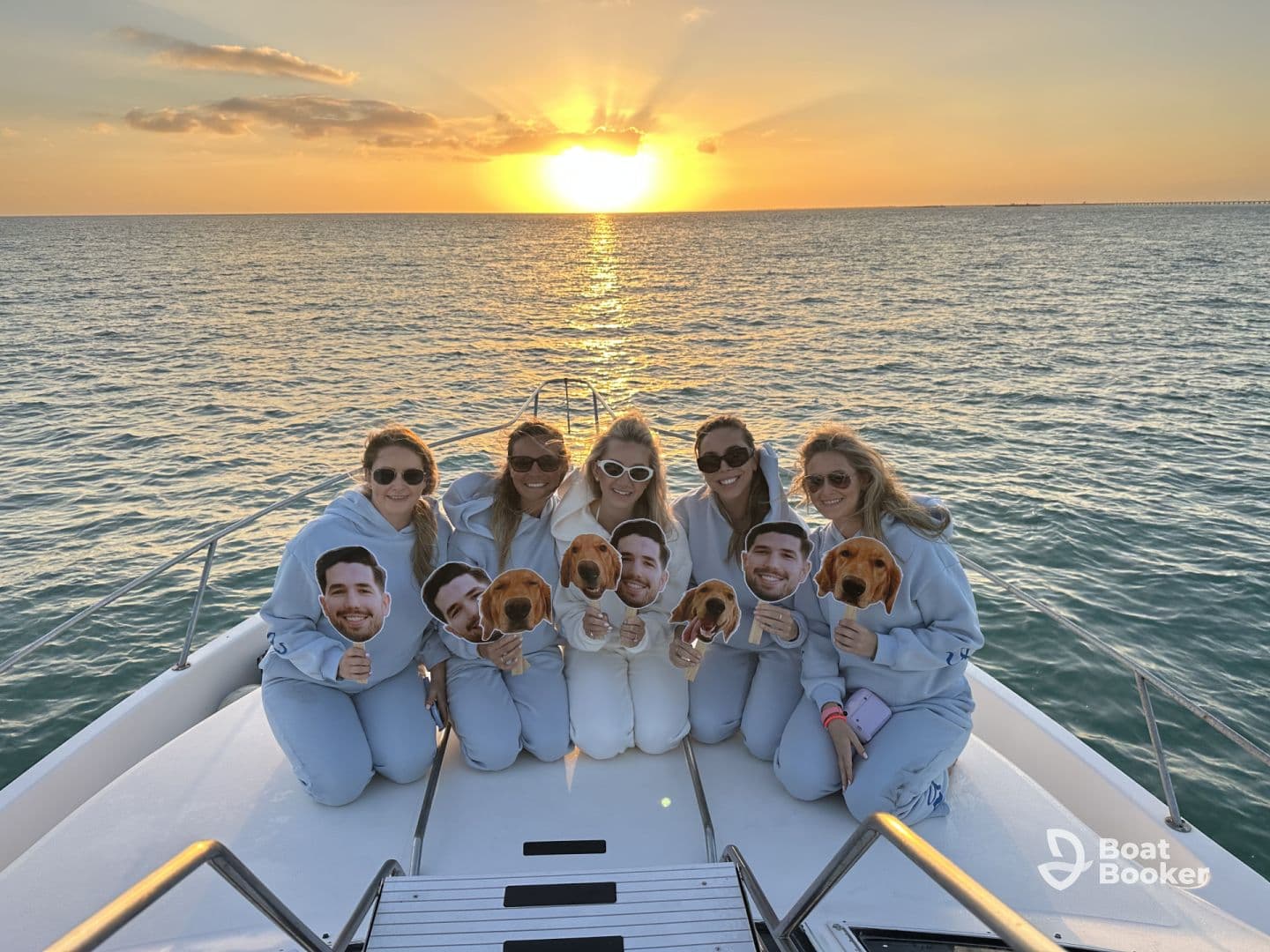A group of friends celebrates at sunset on a yacht, holding playful masks — a perfect moment for fun and memories on the water.