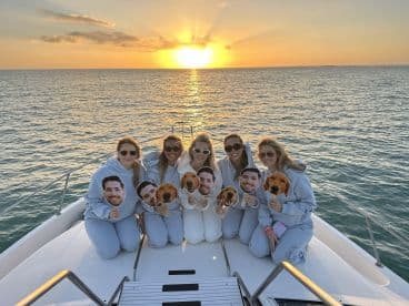 A group of friends celebrates at sunset on a yacht, holding playful masks — a perfect moment for fun and memories on the water.