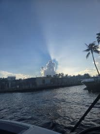 A stunning view of the coastline at sunset, featuring dramatic cloud formations and palm trees, perfect for capturing the beauty of a boating experience.