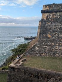 A couple enjoys the scenic view from a historic fort overlooking the ocean, capturing a moment of tranquility amidst stunning coastal scenery.