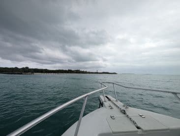 A serene view from the bow of a boat, showcasing the tranquil waters and distant shoreline under a cloudy sky — perfect for exploring coastal destinations.