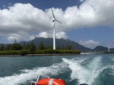 A scenic view of wind turbines along the coastline, captured from a boat navigating through a tranquil waterway — a perfect representation of eco-friendly tourism.