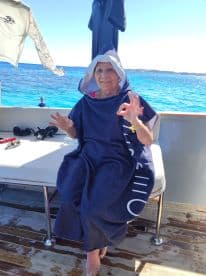 A cheerful elderly woman relaxes on a boat, showcasing a cozy interior space with a beautiful ocean backdrop — perfect for enjoying a day on the water.