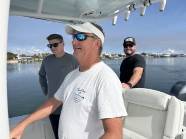 Three friends enjoy a day on the water, with one at the helm of the boat, showcasing a perfect day for boating adventures.