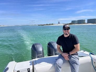 A man enjoys a sunny day on the water, showcasing the beauty of boating with a scenic backdrop of the coastline.