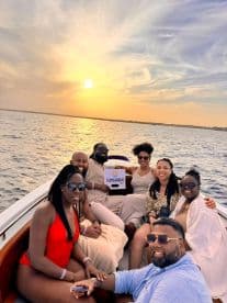 A joyful group enjoys a sunset boat party, capturing memorable moments against a stunning backdrop of the setting sun over the water.
