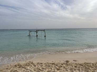 A serene beach scene featuring a wooden structure in the water, with boats visible in the distance. The tranquil atmosphere captures the essence of a relaxing coastal getaway.