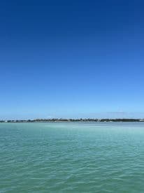A scenic view of calm waters under a clear blue sky, showcasing the tranquil beauty of the coastline.