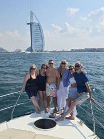 A cheerful group poses on the bow of a boat in Dubai, with the iconic Burj Al Arab in the background — a perfect snapshot of a fun day on the water.