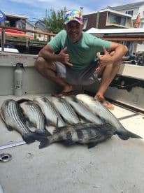 A proud angler poses with a successful catch of striped bass aboard a boat, showcasing the thrill of fishing adventures.