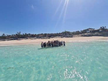 A lively group gathers in the shallow turquoise waters of a beautiful beach, celebrating together under the sun — perfect for memorable outings and group adventures.