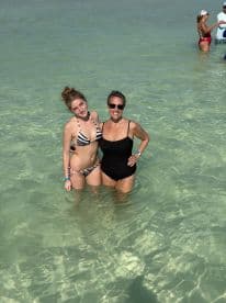 A joyful moment captured with a mother and daughter enjoying a swim in the clear waters, surrounded by friends — perfect for memorable beach outings.