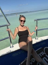 A woman enjoys the sun on the deck of a boat, with clear turquoise waters in the background — a perfect setting for a relaxing day on the water.