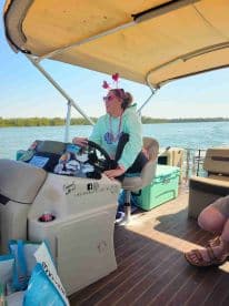 A woman joyfully steers a pontoon boat from the helm, showcasing the vibrant interior and relaxed atmosphere perfect for a day on the water.