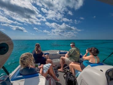 A group of friends enjoys a scenic boat ride over crystal-clear waters, capturing memories with their cameras while soaking up the sun.