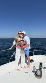 A joyful couple celebrates on the deck of a boat, holding a bouquet of flowers against the backdrop of the ocean — perfect for romantic getaways or special occasions.