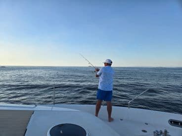 A man enjoys a peaceful fishing experience aboard a boat, casting his line into the serene waters — perfect for fishing enthusiasts seeking adventure on the open sea.