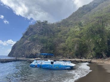 A colorful speedboat is docked near a scenic beach, surrounded by lush greenery and rocky cliffs, perfect for exploring coastal destinations.