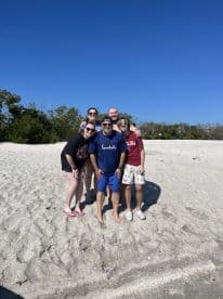 A cheerful group poses together on the beach, capturing a fun moment during their trip — perfect for celebrating special occasions or enjoying a day in the sun.
