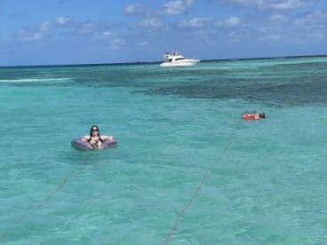 A woman relaxes on a float in crystal-clear waters, with a boat in the background — a perfect scene for a day of fun and relaxation at the beach.