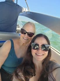 Two women enjoy a sunny day on a boat, capturing a joyful selfie with the beautiful water in the background — perfect for memorable outings on the water.