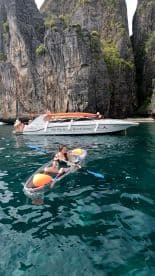 A woman enjoys kayaking in the stunning waters of the Phi Phi Islands, with a scenic backdrop of towering cliffs and a nearby boat, capturing the essence of adventure on the water.